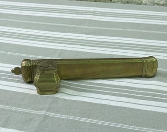 May include: A vintage brass inkwell and pen holder. The inkwell is a small, ornate container with a lid, and the pen holder is a long, rectangular trough. Both pieces feature decorative floral and geometric patterns.
