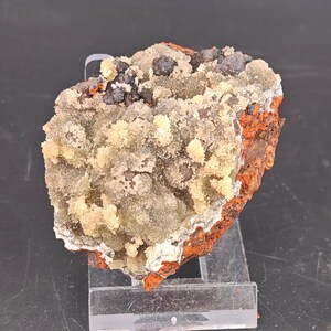 May include: A mineral specimen featuring a cluster of pale yellow and translucent crystalline formations atop a dark, porous, reddish-brown iron-rich matrix. The specimen is displayed on a clear acrylic stand, showcasing its textured surface.
