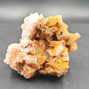 Könnte beinhalten: Ein Cluster aus Naturkristallen mit einer Mischung aus Farben. Die Kristalle haben einen hellen Pfirsichton mit Bereichen in Orange und Braun. Die Gesamtform ist unregelmäßig, mit mehreren sichtbaren Kristallformationen. Die Oberfläche hat ein raues, strukturiertes Aussehen.