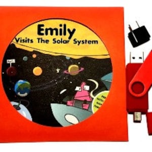 May include: An orange book cover with the title "Emily Visits The Solar System" surrounds a circular illustration of planets and a cartoon character in a spaceship. A red USB drive and a black power adapter are also visible.