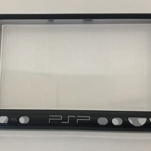 May include: Black plastic shell for a Sony PlayStation Portable (PSP) handheld gaming console. The shell has all the buttons and ports, but no screen.