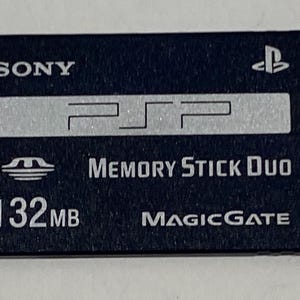 May include: A black Sony PSP Memory Stick Duo with a silver logo and the text "MEMORY STICK DUO" and "MAGICGATE". The memory stick is 32 MB.