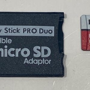 May include: Two memory cards: a black Memory Stick PRO Duo adapter and a red and white microSD card. The adapter is labeled "micro SD Adaptor" and "Memory Stick PRO Duo compatible." The microSD card is labeled "KOOTION" and "32".