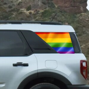 May include: A silver Ford Bronco Sport with a rainbow pride flag decal on the rear window.