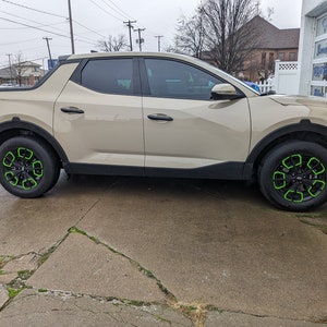 May include: A beige pickup truck with green accents on the wheels. The truck is parked on a concrete surface.