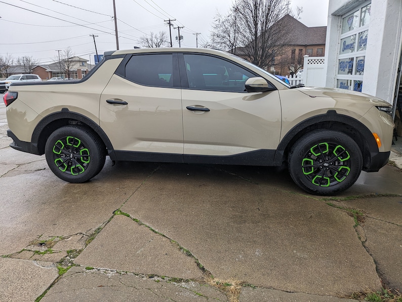 May include: A beige pickup truck with green accents on the wheels. The truck is parked on a concrete surface.