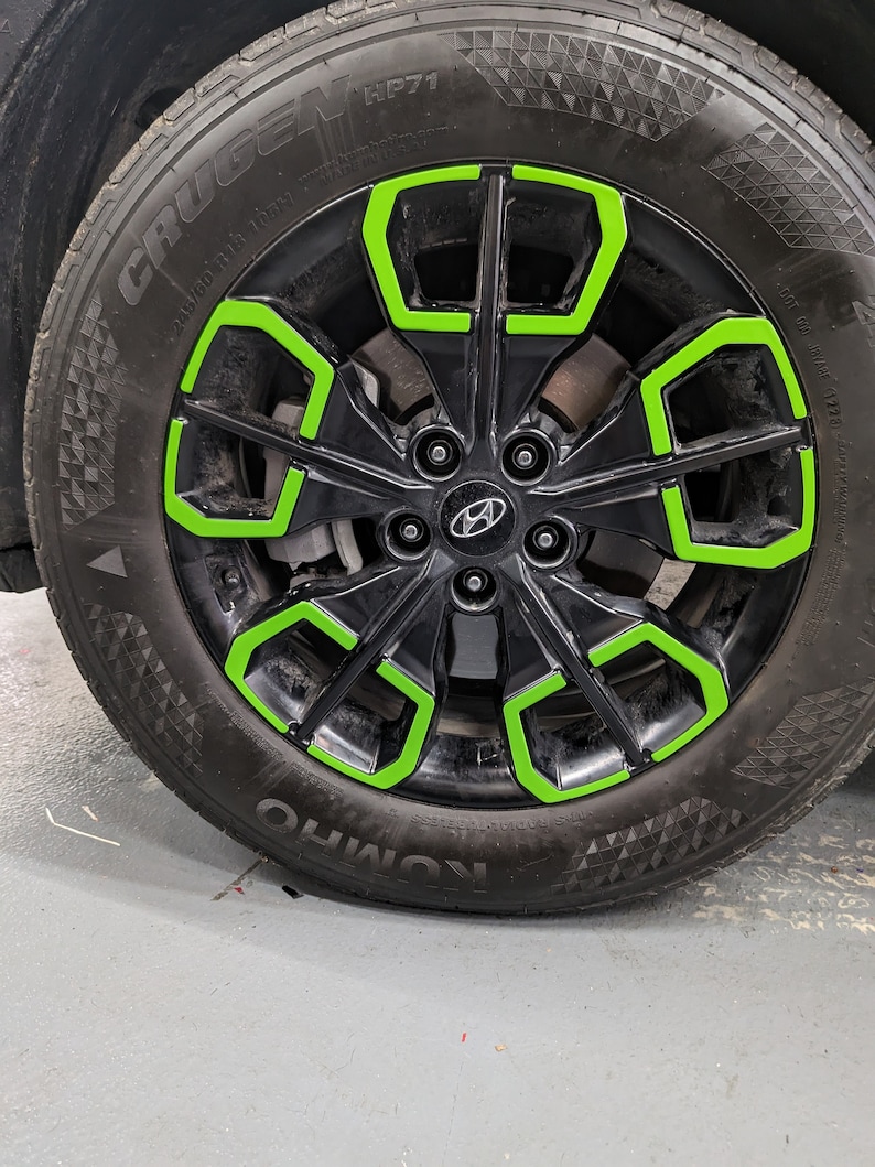 May include: A black car tire with a green rim. The tire has the words "CRUGEN HP71" and "KUMHO" printed on the side.