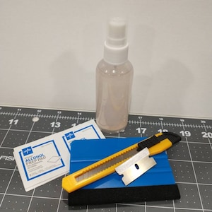 May include: A set of tools for applying vinyl decals, including a blue squeegee, a yellow utility knife, two alcohol prep pads, and a clear spray bottle.