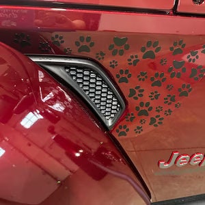 May include: Black paw print decals on a red car door. The decals are arranged in a cluster and are a popular design for car customization.