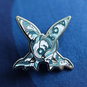 Op de afbeelding: Een zilveren emaille pin met een blauw en wit ontwerp van een gestileerde vogel met uitgespreide vleugels. De vogel is omringd door een golfpatroon.