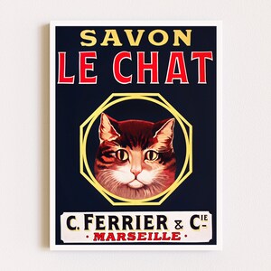 May include: Vintage French soap advertisement featuring a cat's face in a yellow octagon with the text "Savon Le Chat C. Ferrier & Cie - Marseille" in red and white.