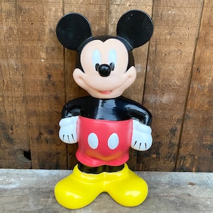 May include: A vintage Mickey Mouse figurine made of plastic. The figurine is black, red, and yellow. Mickey is standing with his hands on his hips and is smiling.