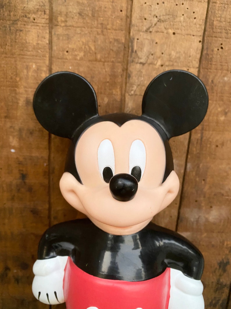 May include: A black and red plastic Mickey Mouse figurine. The figurine is standing with its arms crossed and has a big smile on its face.