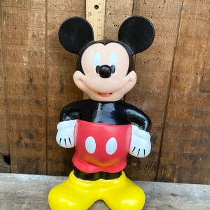 May include: A vintage plastic Mickey Mouse figurine. The figurine is black, red, and yellow. Mickey is standing with his hands on his hips.