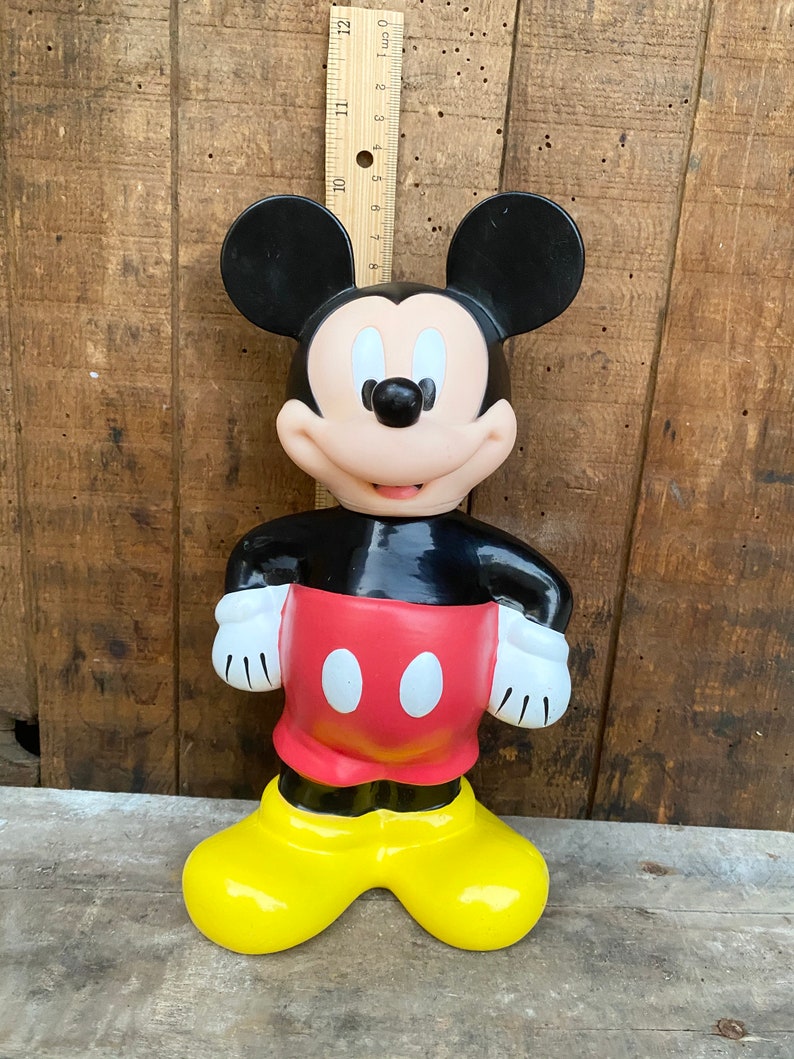 May include: A vintage plastic Mickey Mouse figurine. The figurine is black, red, and yellow. Mickey is standing with his hands on his hips.