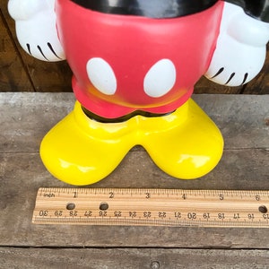 May include: A red and black ceramic Mickey Mouse figurine with yellow shoes. The figurine is approximately 5 inches tall.