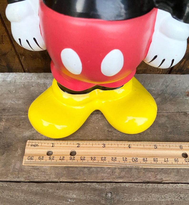 May include: A red and black ceramic Mickey Mouse figurine with yellow shoes. The figurine is approximately 5 inches tall.