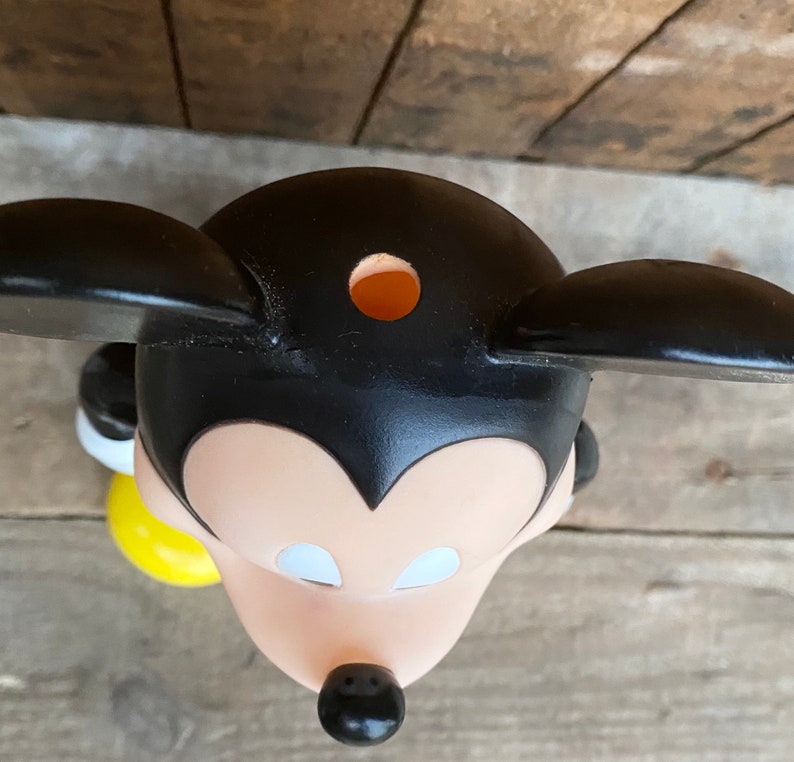 May include: Black and white plastic Mickey Mouse figurine with a yellow base. The figurine has a hole in the top of its head.