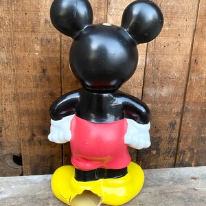May include: A vintage black and red Mickey Mouse figurine with yellow shoes. The figurine is made of plastic and has a chipped shoe.