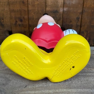 May include: Yellow and red plastic Mickey Mouse bath toy. The toy has a red shirt with black outlines and two white circles. The toy's feet are yellow and have the following text: "DISNEY MPG by Monogram Products Inc. Largo, Florida 34649 MADE IN CHINA NOT DISHWASHER SAFE WASH THOROUGHLY BEFORE USING WASH IN WARM WATER ONLY AVOID TEMPERATURE EXTREMES"