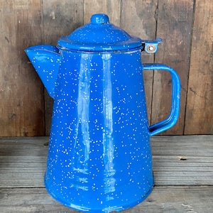 May include: A blue enamel coffee pot with white speckles. The pot has a lid with a handle and a spout.