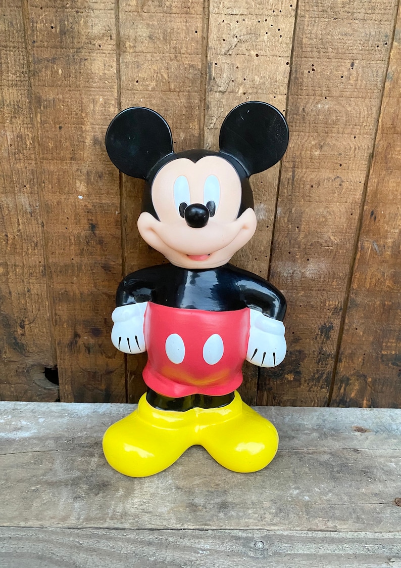 May include: A vintage Mickey Mouse figurine made of plastic. The figurine is black, red, and yellow. Mickey is standing with his hands on his hips and is smiling.