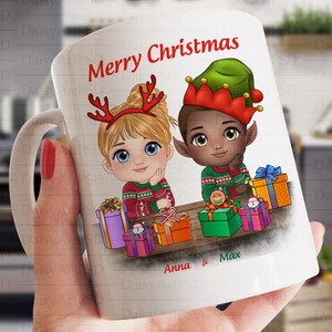 May include: White ceramic mug with a Christmas theme. The mug features a cartoon illustration of a girl with blonde hair wearing a red sweater and a boy with brown skin wearing a green elf hat and a red sweater. The mug has the text "Merry Christmas" and "Anna & Max" printed on it.