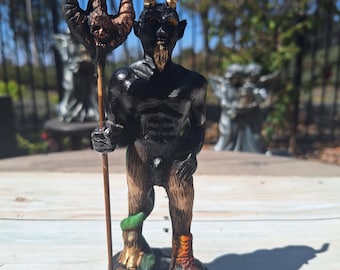 May include: A black and gold figurine of a horned demon holding a trident. The demon has a muscular build and is standing on a black base with gold stars.