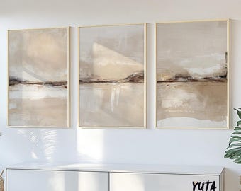 May include: Three abstract landscape paintings in beige, brown, and white tones. The paintings are framed in gold and hung on a white wall above a white cabinet.