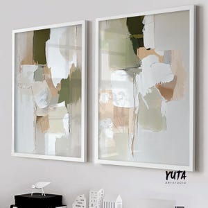 Peut inclure: Deux œuvres d'art abstraites encadrées. Chaque œuvre présente un mélange de coups de pinceau blancs, beiges et vert olive. Les peintures sont dans des cadres blancs et sont affichées sur un mur. Le texte "YUTA ARTSTUDIO" est dans le coin inférieur droit.