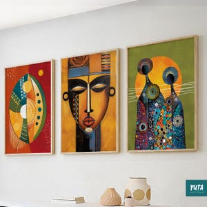 May include: Three framed abstract art prints. The artwork features bold colours and geometric shapes, including a face and figures. The frames are a light wood colour. The art is displayed on a white wall.