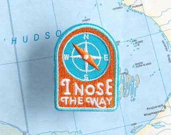 May include: A blue and orange embroidered patch with a compass and the text "I nose the way".