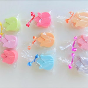Può includere: Assortimento di nove saponi colorati a forma di tulipano avvolti in plastica trasparente con un nastro legato attorno a ciascuno. I saponi sono in tonalità di rosa, arancio, giallo, verde, blu e viola.