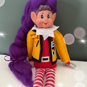 May include: A doll with a smiling face, large purple hair, and elf-like ears. The doll wears a yellow jacket over a red shirt, red and white striped trousers, and a white collar. The doll has a silver accessory in its right hand.