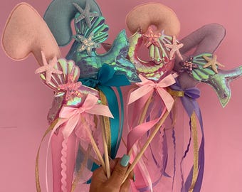 Puede incluir: Tres varitas con temática de sirena con colas de sirena iridiscentes, conchas y estrellas de mar. Cada varita tiene un número de fieltro rosa, azul o morado, y está coronada con una cinta rosa, azul o morada.