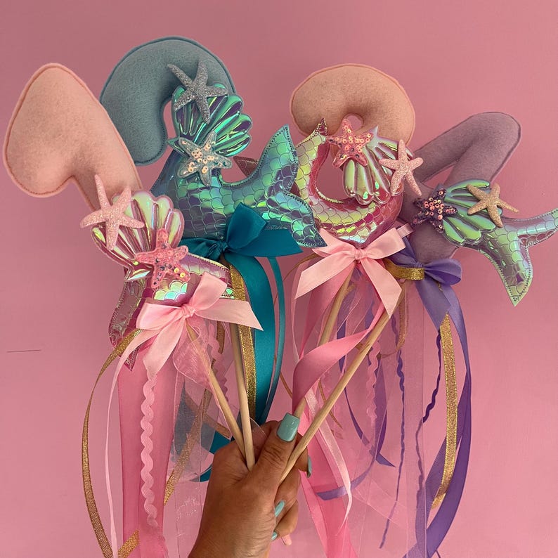 May include: Three mermaid-themed wands with iridescent mermaid tails, seashells, and starfish. Each wand has a pink, blue, or purple felt number, and is topped with a pink, blue, or purple ribbon.