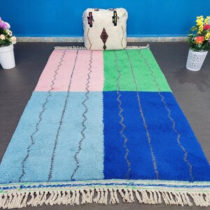 May include: A colorful Moroccan rug with a pink, blue, green, and blue pattern. The rug has a fringe border and is made of wool.