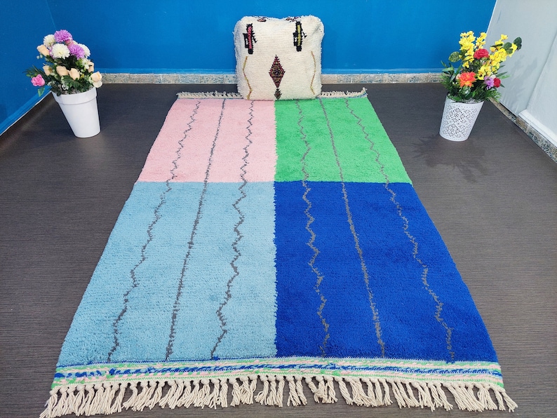 May include: A colorful Moroccan rug with a pink, blue, green, and blue pattern. The rug has a fringe border and is made of wool.