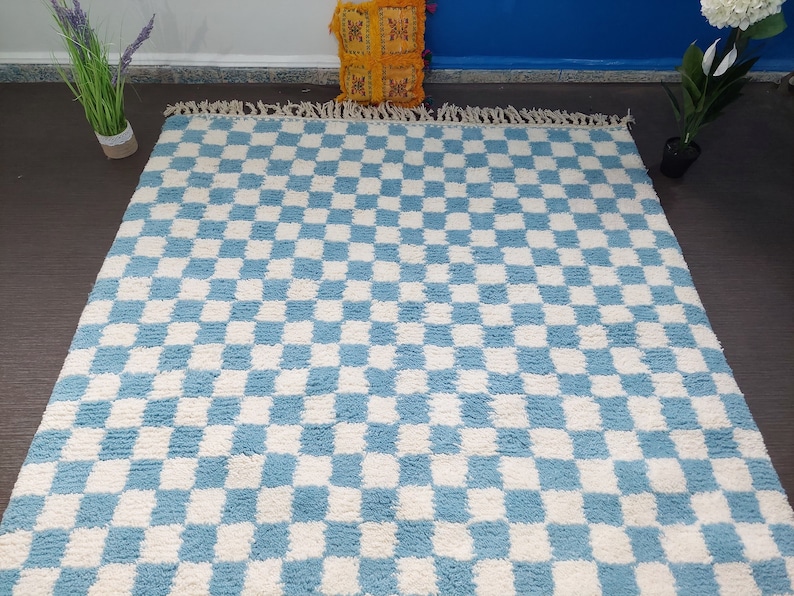 May include: A blue and white checkered rug with a fluffy texture. The rug has a fringe border.