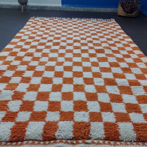 Op de afbeelding: Een groot, rechthoekig vloerkleed met een dambordpatroon van oranje en witte vierkanten. Het vloerkleed heeft een dikke, getextureerde pool en een gefranjerde rand. Afmetingen zijn ongeveer 200 cm x 300 cm.