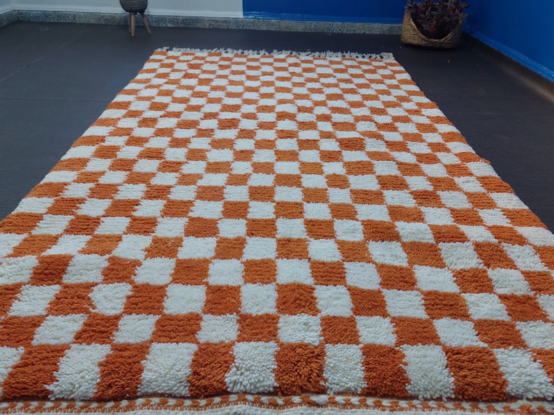 Op de afbeelding: Een groot, rechthoekig vloerkleed met een dambordpatroon van oranje en witte vierkanten. Het vloerkleed heeft een dikke, getextureerde pool en een gefranjerde rand. Afmetingen zijn ongeveer 200 cm x 300 cm.