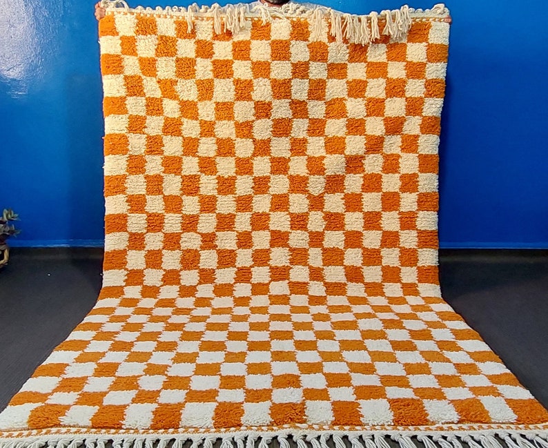 Op de afbeelding: Een groot, rechthoekig vloerkleed met een dambordpatroon in oranje en cr&egrave;me. Het vloerkleed heeft een dikke, getextureerde pool en een franje langs de randen. Geschikt voor een woon- of slaapkamer, afmetingen zijn ongeveer 200 cm x 300 cm.