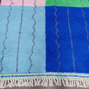 May include: A colorful woven rug with a geometric pattern in shades of blue, green, and pink. The rug has a fringe border.
