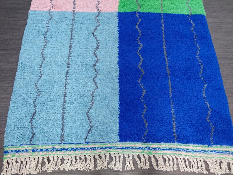 May include: A colorful woven rug with a geometric pattern in shades of blue, green, and pink. The rug has a fringe border.