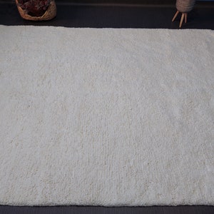 May include: A white shag rug with a fringe border. The rug is made of soft, fluffy fibers and has a subtle texture.