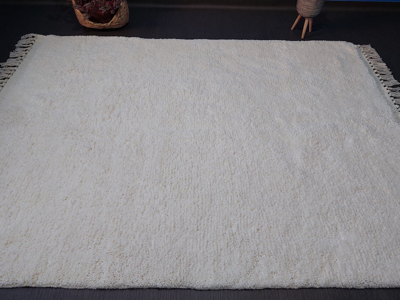 May include: A white shag rug with a fringe border. The rug is made of soft, fluffy fibers and has a subtle texture.