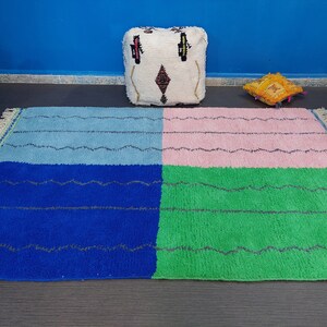 May include: A colorful Moroccan rug with a blue, green, pink, and light blue pattern. The rug has a fringe border and is made of wool.