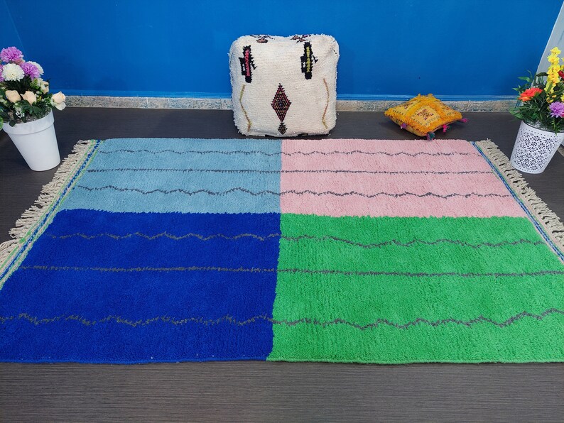 May include: A colorful Moroccan rug with a blue, green, pink, and light blue pattern. The rug has a fringe border and is made of wool.