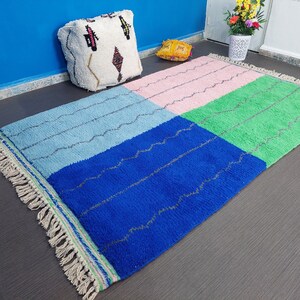 May include: A colorful Moroccan rug with a blue, green, pink, and light blue geometric pattern. The rug has a fringe border and is made of wool.