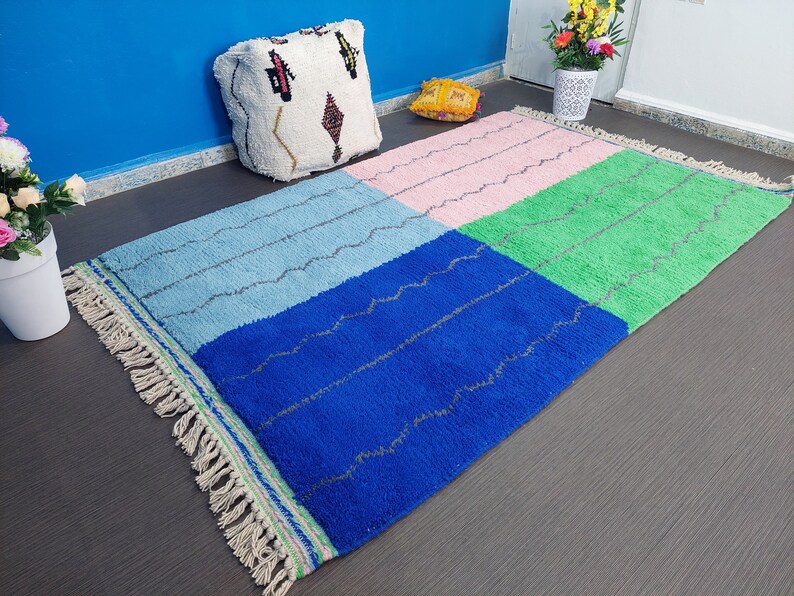 May include: A colorful Moroccan rug with a blue, green, pink, and light blue geometric pattern. The rug has a fringe border and is made of wool.